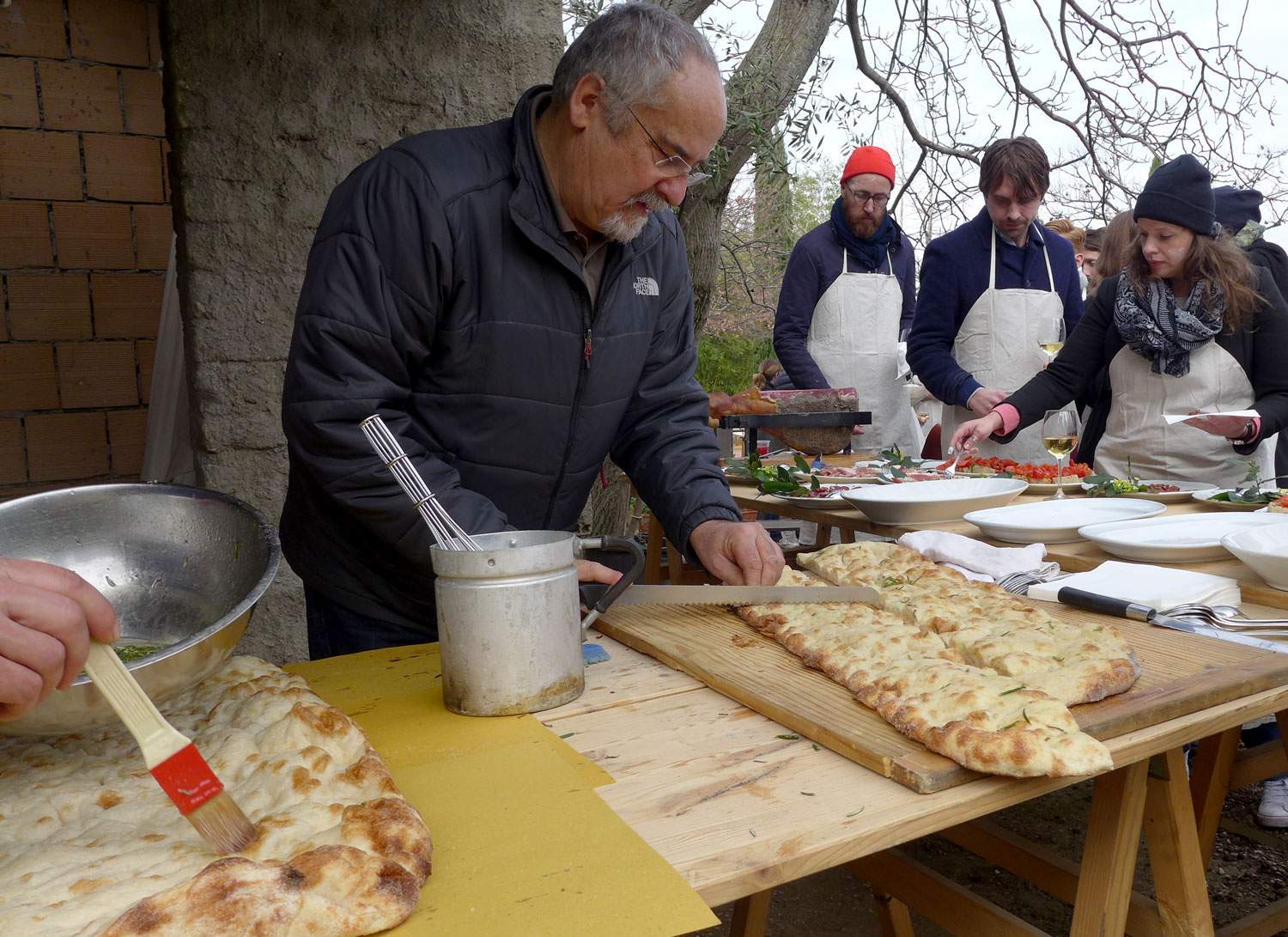 Noen pensler pizzaene og noen skjærer ferdig rosmarinpizza som skal serveres sammen med herlige råvarer.